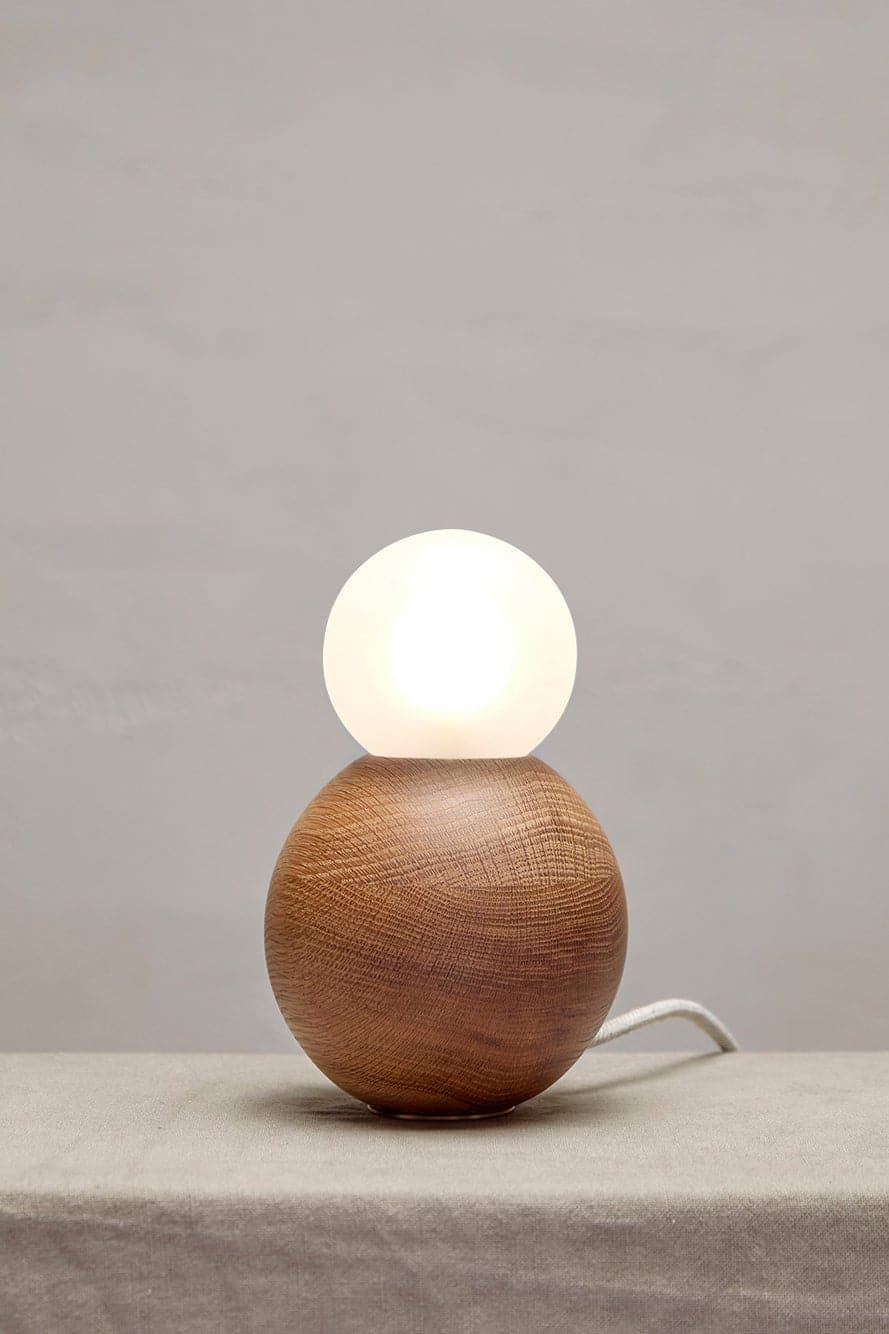 Marz Designs Bright Beads Sphere Table Lamp in Oak with the light on.